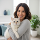 Smiling woman in her 30s with a short-haired cat, blurred living room background in slate blue and white.
